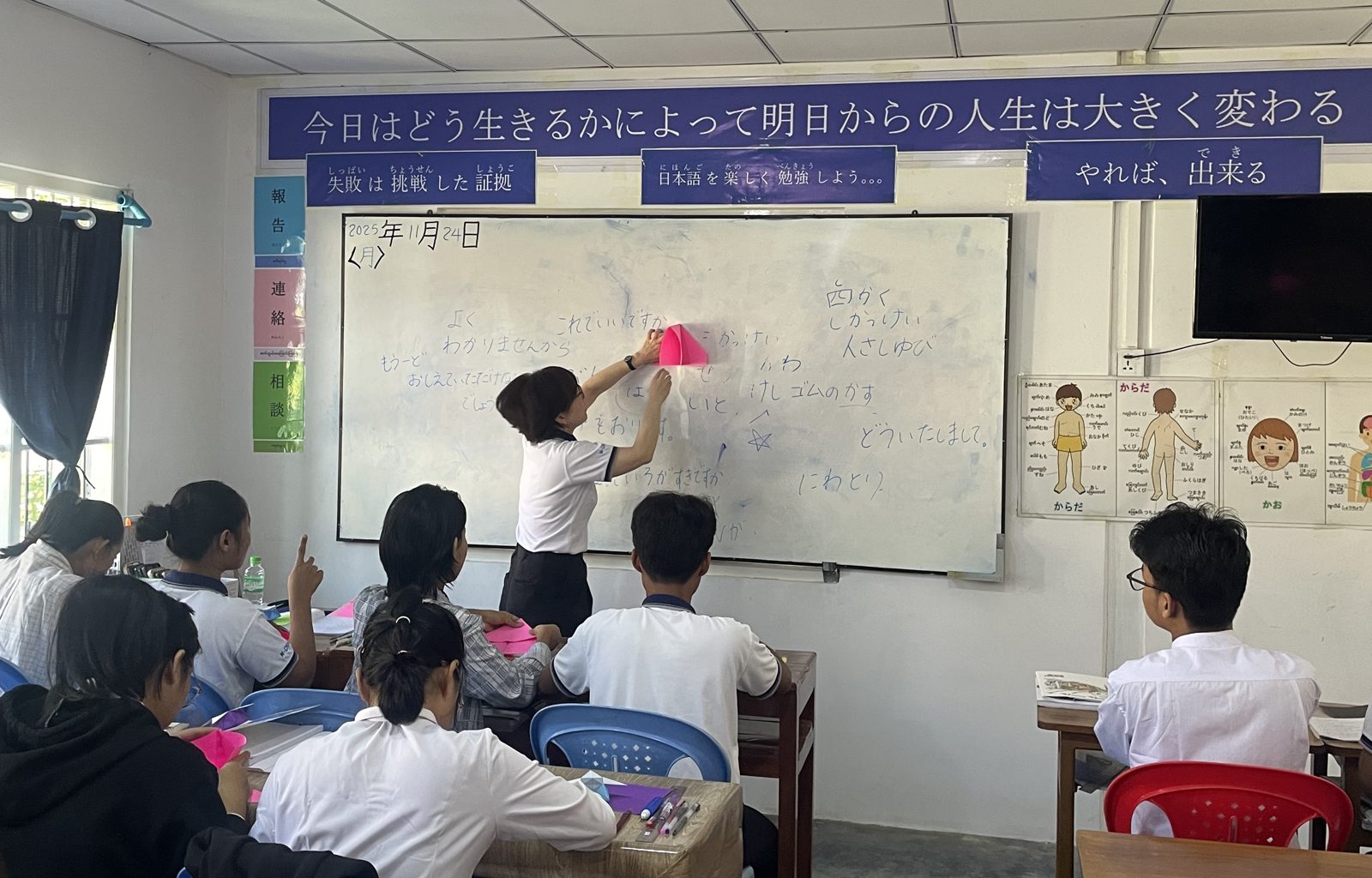 ミャンマー現地校の教室。講師がホワイトボードの前で折り紙を使って説明している